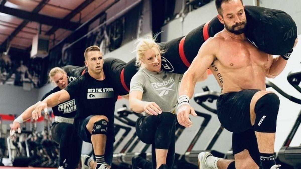 Team CrossFit Mayhem performing a set of walking lunges with a large sandbag resting on all four team member's shoulders