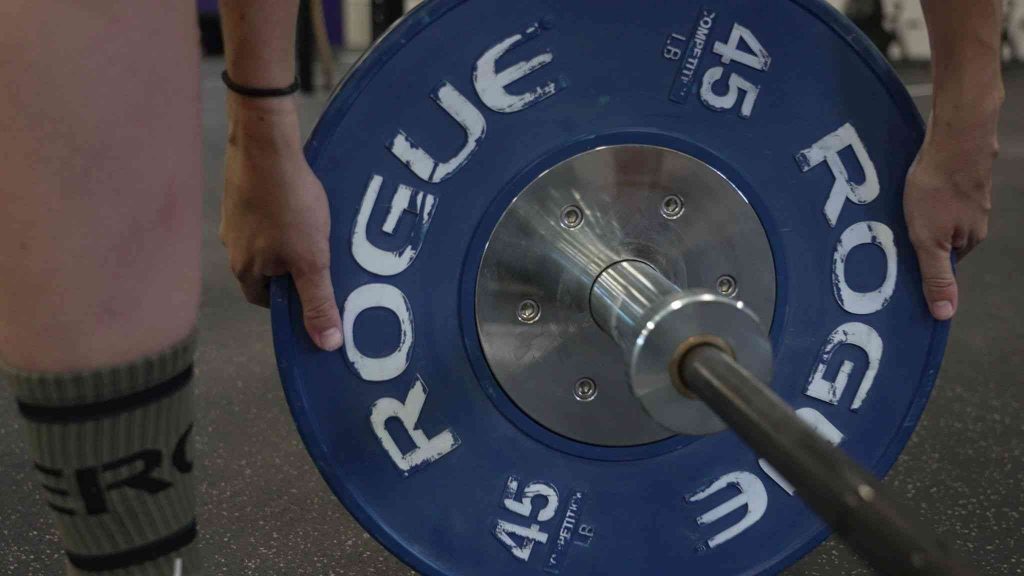 A woman sliding a 45-pound bumper plate onto a barbell