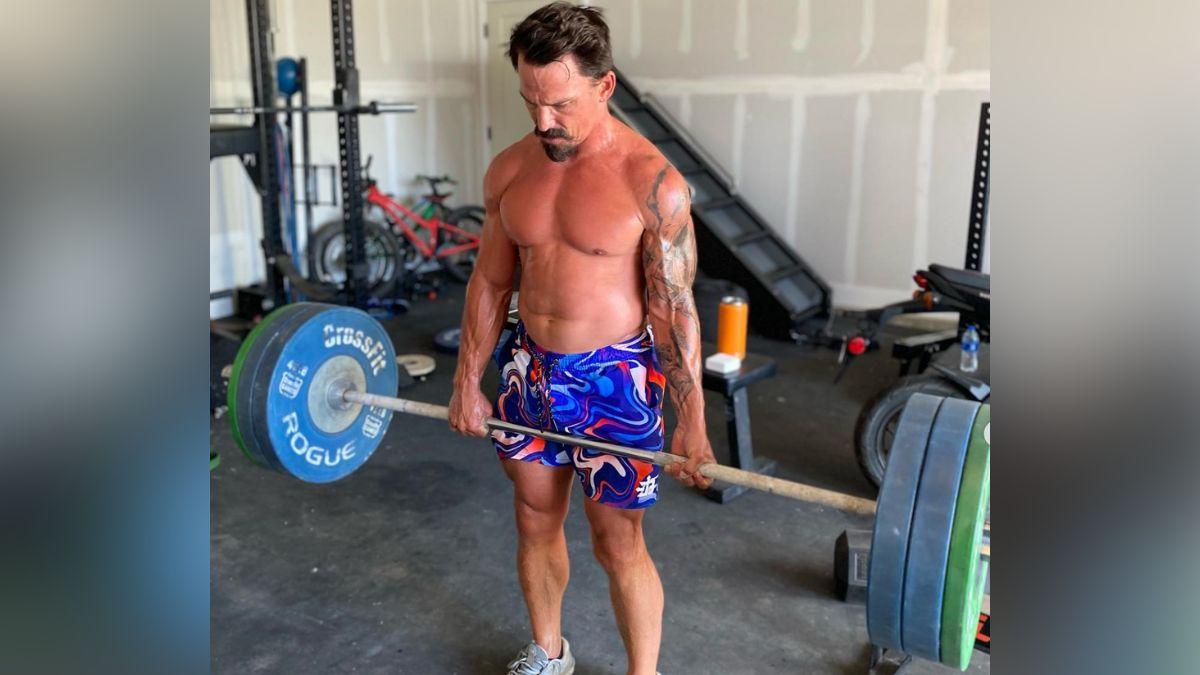 CrossFitter Josh Bridges deadlifting a loaded barbell off of the floor. He's wearing brightly colored shorts.