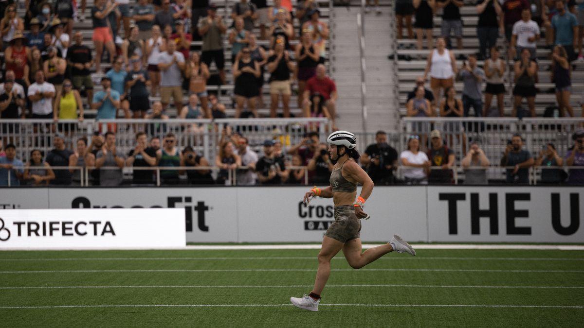 CrossFitter Mal O'Brien sprints down a grass field wearing green shorts and sports bra and a bike helmet.
