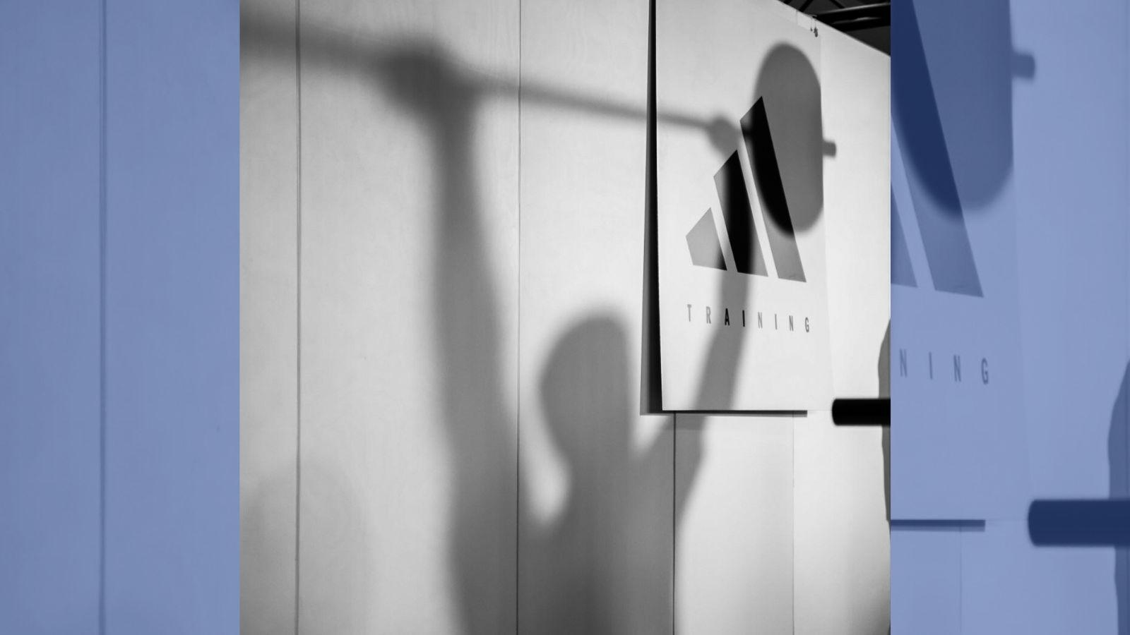 The shadow of a person lifting a barbell is cast across an adidas logo titled "training".